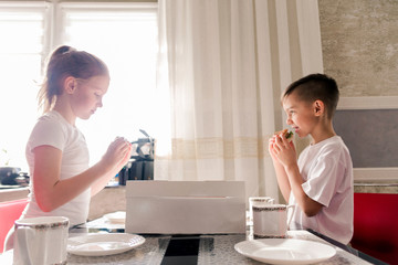 Food delivery. Boy and girl, brother and sister at home in the kitchen eat mini burgers out of the box.