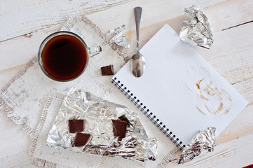 A cup of coffee, chocolate, a sheet of paper and a pen on a white wooden surface. Background for...