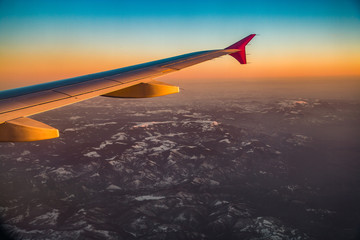 Airplane wings in sunset over mountains