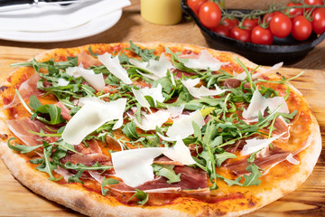 Fresh oven baked traditional prosciutto, rucola, tomato and parmesan pizza, served on a wooden board
