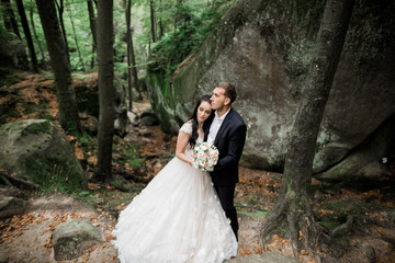 Romantic, fairytale, happy newlywed couple hugging and kissing in a park, trees in background