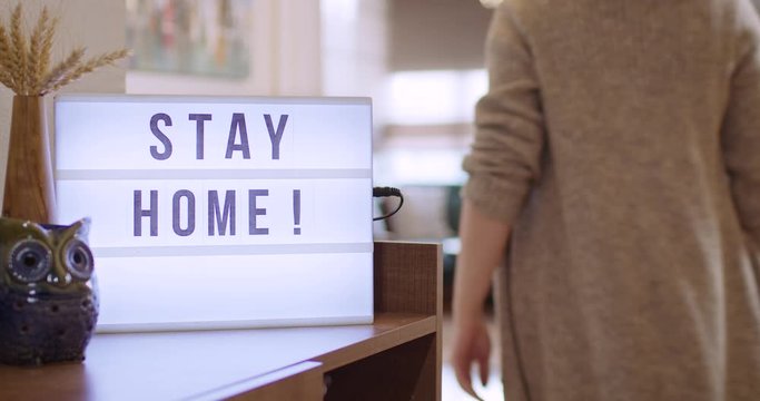 Woman walks in and Switches on Decorative Lightbox Written Stay Home in Comfy and Cozy Home