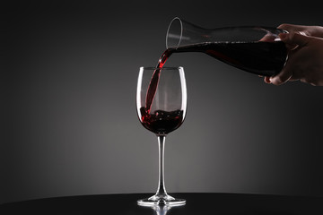 Pouring of tasty wine from decanter into glass on dark background