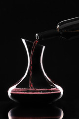Pouring of tasty wine from bottle into glass on dark background
