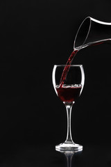 Pouring of tasty wine from decanter into glass on dark background