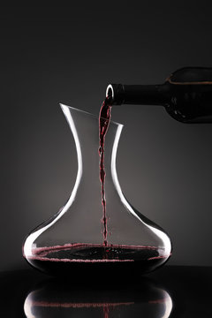 Pouring of tasty wine from bottle into glass on dark background