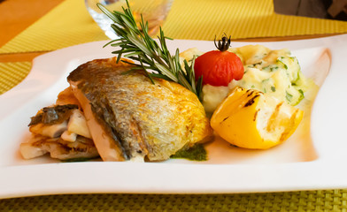 White fish fillet with puree served with lemon and rosemary in a white plate, restaurant setting