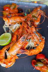 Sauteed shrimps in tomato, capers and olives sauce. Black plate in a restaurant setting background