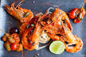 Sauteed shrimps in tomato, capers and olives sauce. Black plate in a restaurant setting background