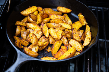 delicious potato wedges in a cast-iron pan on a grill as side dish to the bbq
