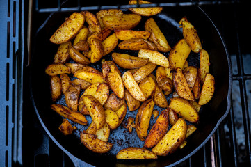 delicious potato wedges in a cast-iron pan on a grill as side dish to the bbq