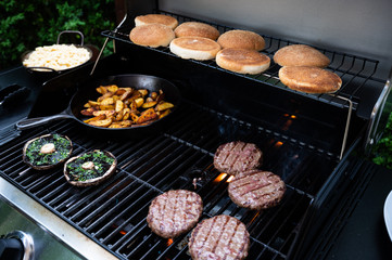 burgers on the bbq grill with potato wedges in pan and giant mushrooms