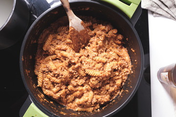 Cooking bolognese pasta fusilli on a black pan with a wooden spoon in a domestic kitchen