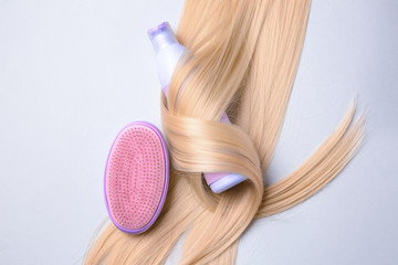 Bottle of shampoo for blonde hair and brush on light background