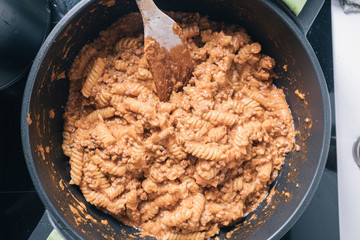 Cooking bolognese pasta fusilli on a black pan with a wooden spoon in a domestic kitchen