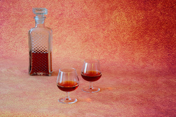 A crystal decanter with a lid and two glasses with cognac stand on a brown abstract background.