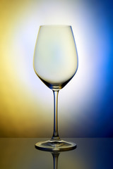 The crystal glass stands on the reflecting surface on a blue yellow background. studio photo. product. Beautiful shadow from wine glass. macro photo