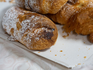Homemade breakfast in the morning. A croissant with icing sugar and chocolate chips served on a paper tray on the table.
