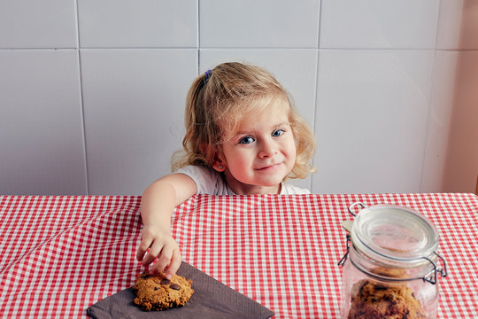 girl picking up a homemade cookie smiling and looking into the camera