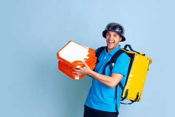Proposing pizza. Emotions of caucasian deliveryman isolated on blue background. Contacless delivery service during quarantine. Man delivers food during isolation. Safety. Hurrying up. Looks fun.