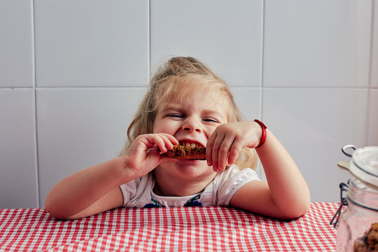 blonde girl eating a homemade cookie on a table with a rustic tablecloth