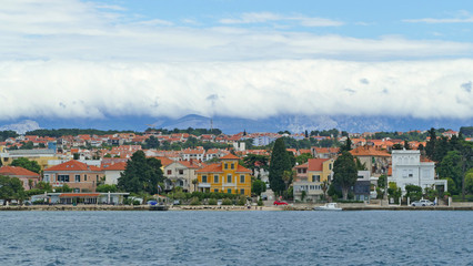 Fototapeta na wymiar Croatian coast with small harbour town and mountains covered with low clouds, Zadar