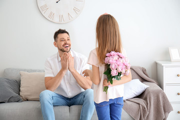 Little daughter holding flowers for her father behind her back at home