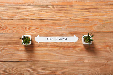 Houseplants with text KEEP DISTANCE on wooden background