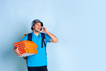 Calling to client. Emotions of caucasian deliveryman isolated on blue background. Contacless delivery service during quarantine. Man delivers food during isolation. Safety. Hurrying up. Looks fun.