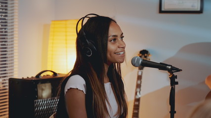 Close-up of beautiful smiling girl in headphone singing her favourite song on the rehearsal in home...