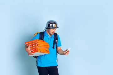 Calling to client. Emotions of caucasian deliveryman isolated on blue background. Contacless delivery service during quarantine. Man delivers food during isolation. Safety. Hurrying up. Looks fun.