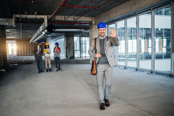 Full length of smiling friendly caucasian real estate agent walking in building in construction process and showing okay sign.