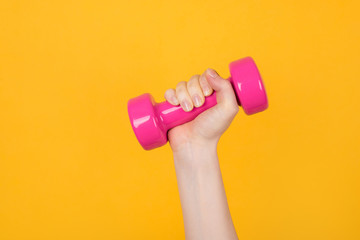 Working out concept. Cropped photo of a sportive woman holding pink dumbbell in her hand isolated on yellow background