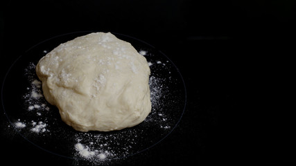 Close-up of dough and flour on a black background. Preparation for pies and rolls. Homemade cakes, cooking. Free space