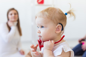 Hearing aid in baby girl's ear. Toddler child wearing a hearing aid at home. Disabled child,...