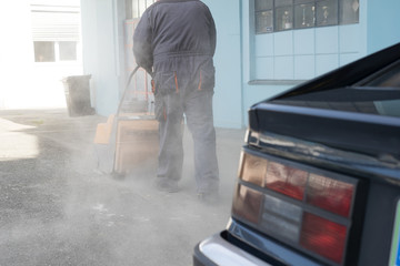 A person is pushing an orange gasoline powered industrial sweeper over dirty asphalt parking lot in an attempt to clean it from debris and sand