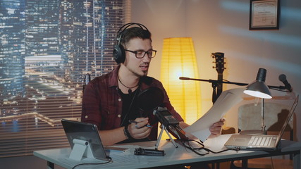 Home recording studio: the speaker in headphone reads the story into the microphone. There is a computer and other recording equipment on the table.