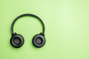Naklejka premium Black headphones on the left side of the photo. From above . Green background. Copy space