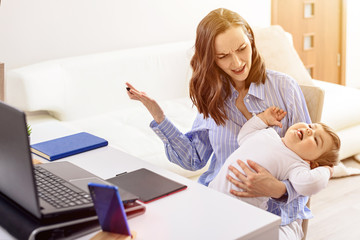 woman in blue shirt with naughty child on lap working at laptop, maternity leave, freelancer,...