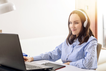 Fototapeta na wymiar happy woman in blue shirt with white headphones listening to music, remote work at home, freelancer, comfortable life