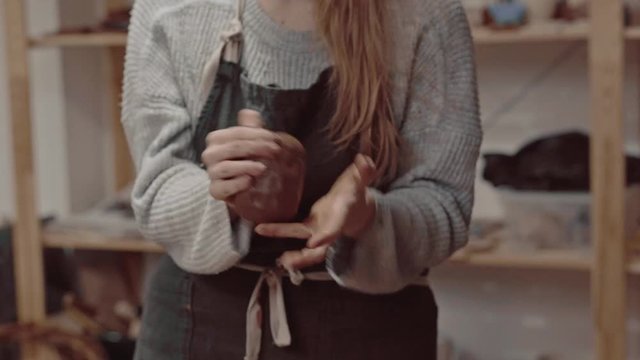 The girl crushes the clay in the hands. Potter's work close-up. Female hands crumple clay closeup.