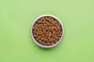 Dog food in a silver bowl. In the center. Green background. Copy, text sapce.