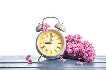 Alarm clock and flowers on table against white background. Spring time