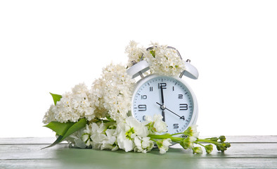 Alarm clock and flowers on table against white background. Spring time