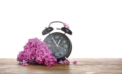 Alarm clock and flowers on table against white background. Spring time