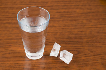 A glass and an ice cube on a wooden table