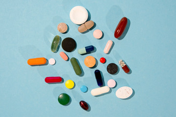 Assorted pharmaceutical medicine pills, tablets and capsules over blue background