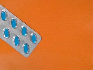 Blue pills in a blister pack on an orange background with copy space.