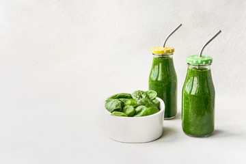Green smoothie with spinach in small bottles and spinach leaves in bowl on white background. Copy space. Healthy lifestyle concept