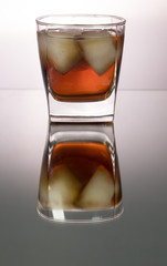 Glass of whiskey with pieces of ice on mirroring table. Vertical image with copy space.